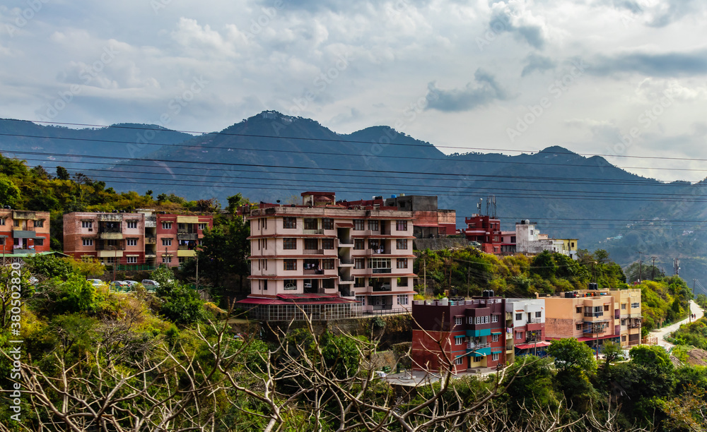 wide shot of buildings on mountain along side road and trees with cloudy sky in the background