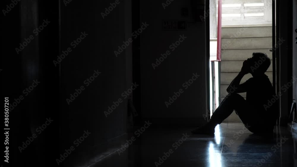 Silhouette of a sad man sitting in the dark leaning against the wall in old condo, Domestic violence, family problems, Stress, violence, The concept of depression and suicide Silhouette of a sad man sitting in the dark leaning against the wall in old condo, Domestic violence, family problems, Stress, violence, The concept of depression and suicide