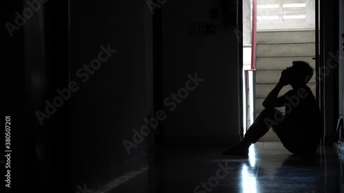 Silhouette of a sad man sitting in the dark leaning against the wall in old condo, Domestic violence, family problems, Stress, violence, The concept of depression and suicide