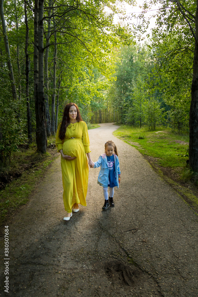 Pregnant woman in yellow dress with her daughter in nature Pregnant woman in yellow dress with her daughter in nature