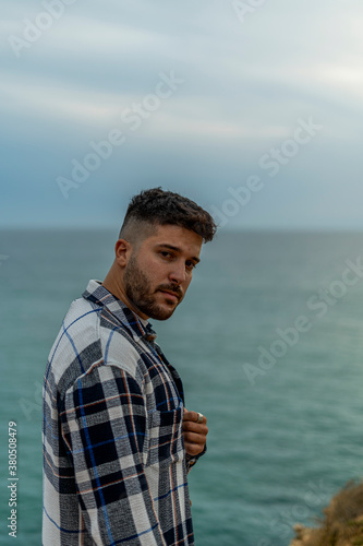 Hombre joven adolescente modelo con camisa azul de cuadros posando en la costa y playa 