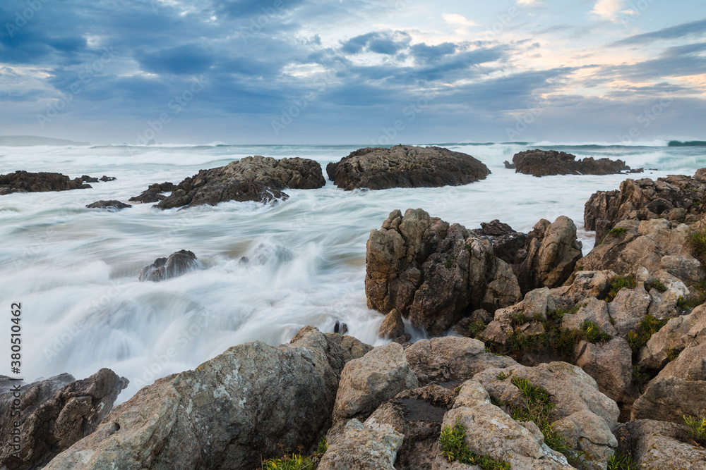 Waves crashing against a rocky shore at sunset Waves crashing against a rocky shore at sunset