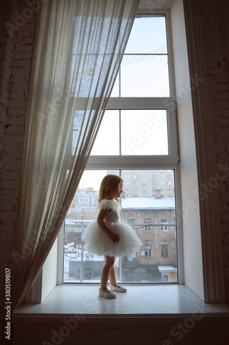 a little girl in a smart, fluffy white dress near the window and waits for Santa Claus or the tooth fairy. children's fairy tales and dreams. new year holiday.