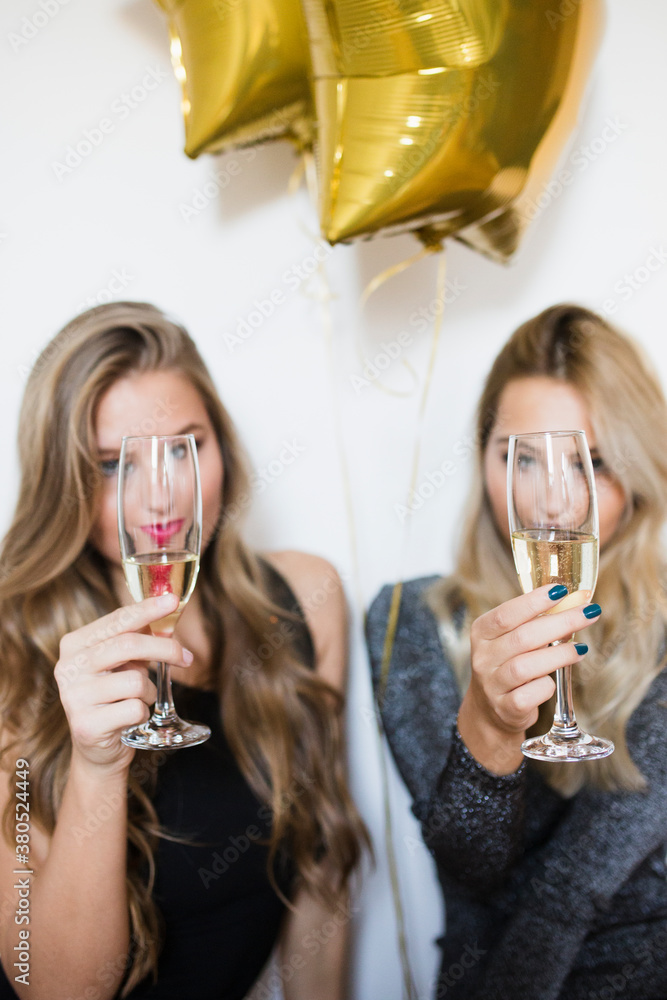 Two female friends holding glasses of champagne in front on their faces Two female friends holding glasses of champagne in front on their faces