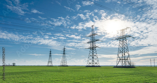 Electrical net of poles on a panorama of blue sky and green meadow