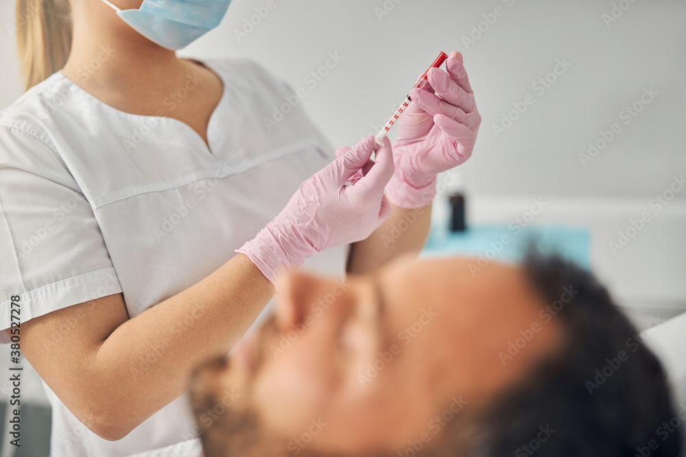 Doctor cosmetologist holding syringe while man lying on daybed Doctor cosmetologist holding syringe while man lying on daybed
