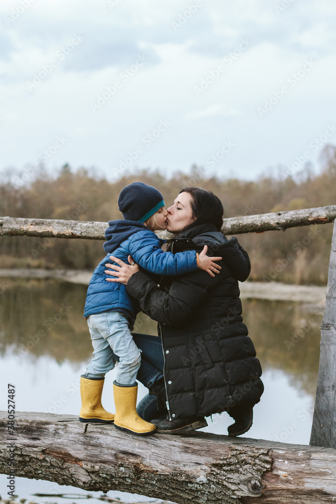 mother and son kissing on a wooden bridge in autumnal landscape mother and son kissing on a wooden bridge in autumnal landscape