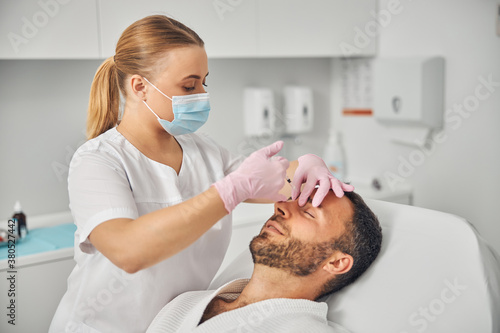 Female doctor cosmetologist making injection in man forehead
