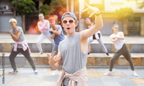 Positive teen boy dancing modern street dance outdoors with teenagers in background.