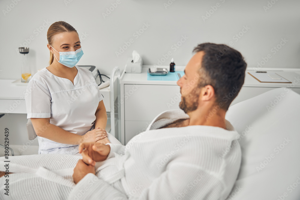 Obraz premium Charming beautician talking with young man in cosmetology cabinet