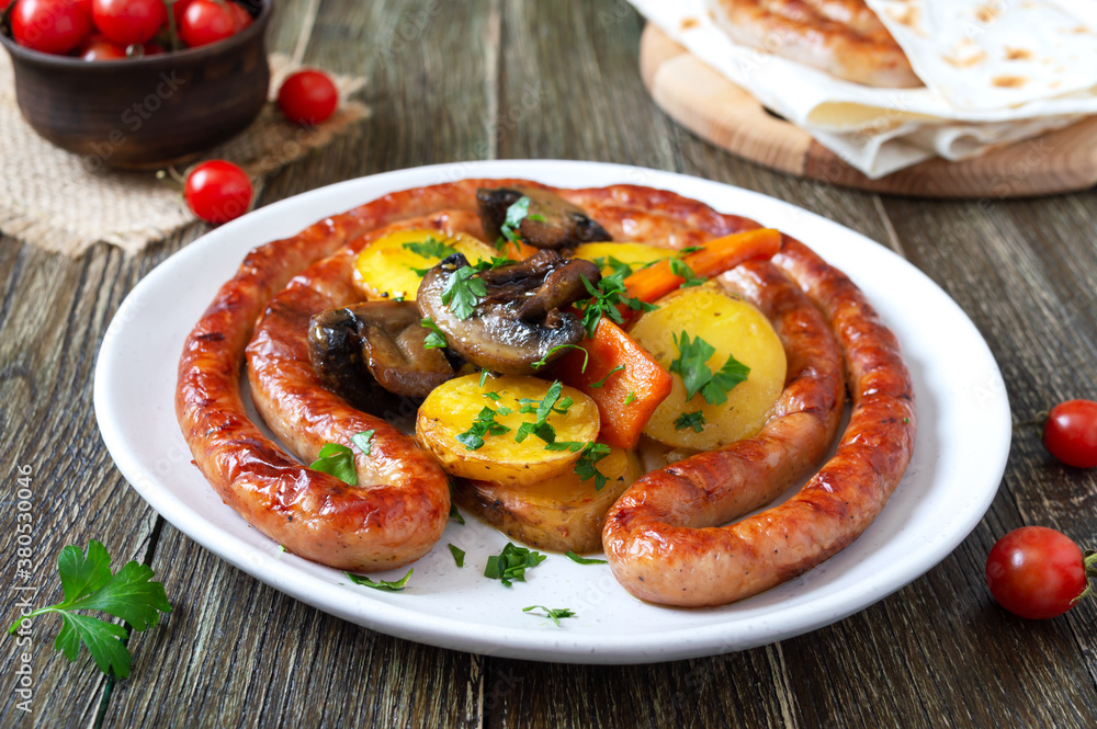 Tasty homemade grilled sausages with baked herb potatoes, mushrooms, cherry tomatoes and ketchup on a wooden background. Oktoberfest snack. Summer picnic dish