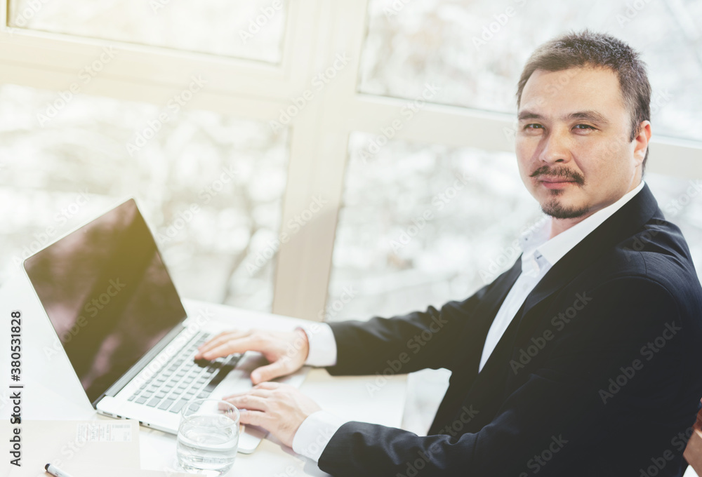 Asian successful businessman sitting at the table with laptop. Panoramic window background. Triumph, happiness. Asian successful businessman sitting at the table with laptop. Panoramic window background. Triumph, happiness.