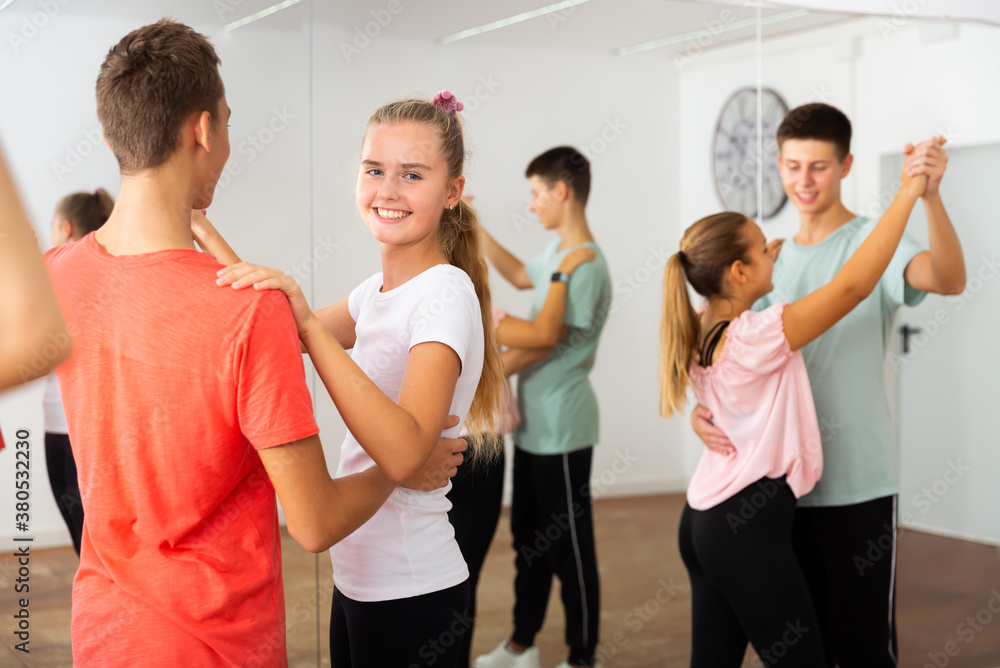 Teens in pairs learning to dance waltz with young female choreographer in modern studio
