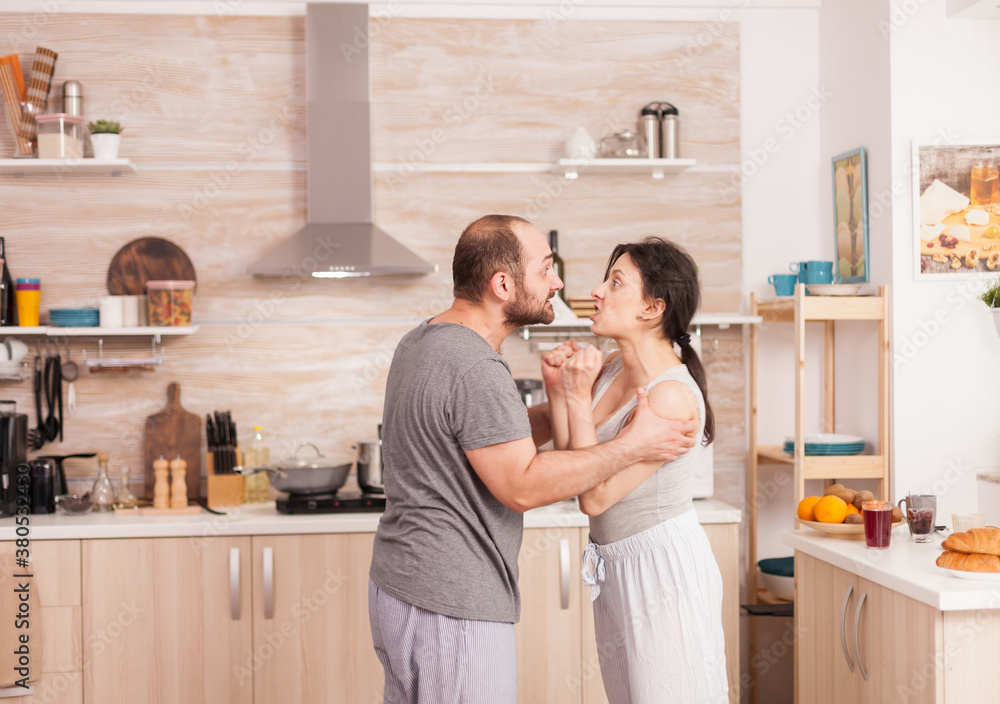 Husband and wife screaming in frustration at each other during breakfast in kitchen. Domestic violence threatening aggressive angry frustrated husband abusing physical depressed sad unhappy crying Husband and wife screaming in frustration at each other during breakfast in kitchen. Domestic violence threatening aggressive angry frustrated husband abusing physical depressed sad unhappy crying