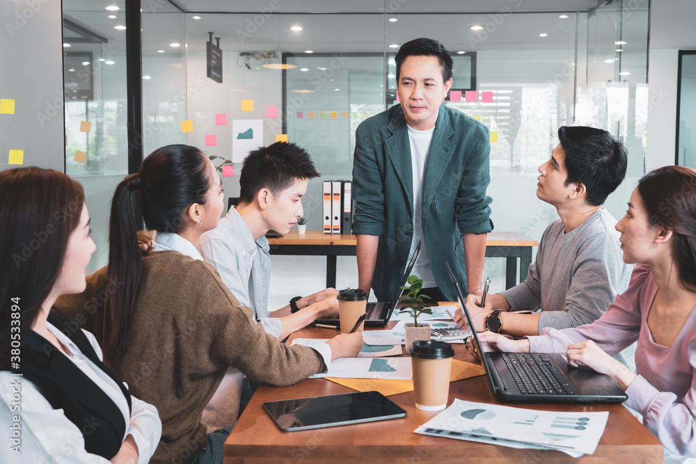 Focus on asian man(boss or manager)standing in group brainstorm meeting in office.Businesspeople discussing with paperwork for business plan,Corporate of modern colleague Focus on asian man(boss or manager)standing in group brainstorm meeting in office.Businesspeople discussing with paperwork for business plan,Corporate of modern colleague