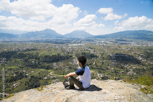Young man sitting on top of the mountain watching the horizon - man meditating in the heights observing the volcano and mountains in front of him