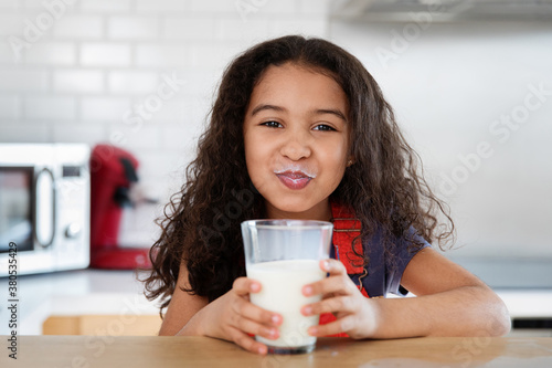 Funny little girl with milk mustache after drinking glass of milk