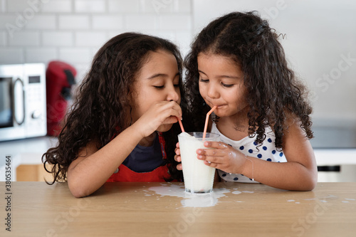 Sisters sharing a glass of milk at kitchen counter photo