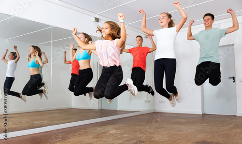 Cheerful teenage boys and girls jumping together while dancing synchronous group choreography in modern dance studio