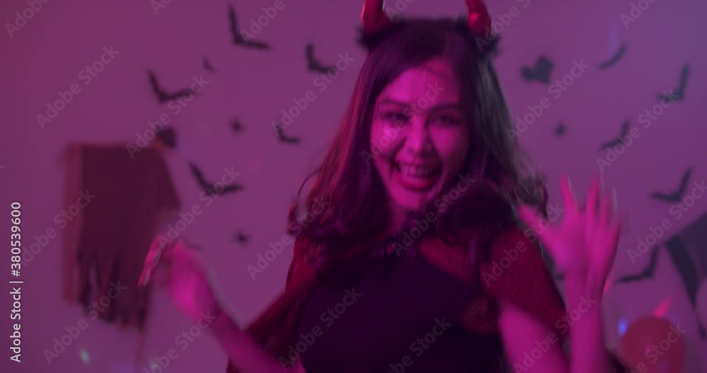Close up, portrait of attractive young asian woman wearing in vampire costume looking at camera smiling and dancing at night halloween party over dark background with colorful light setting. Close up, portrait of attractive young asian woman wearing in vampire costume looking at camera smiling and dancing at night halloween party over dark background with colorful light setting.