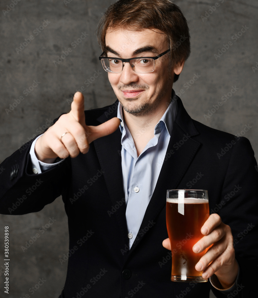 Middle-aged man in stylish official clothing jacket and shirt holds a glass of drink craft beer and points finger at camera Middle-aged man in stylish official clothing jacket and shirt holds a glass of drink craft beer and points finger at camera