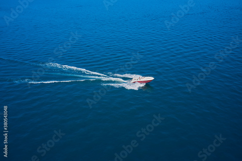 The boat is combined in red in the rays of the sun on blue water. Top view of a white boat sailing to the blue sea.