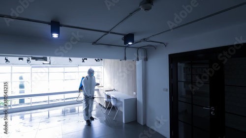 Worker in personal protective equipment (ppe) suit cleaning in building with spray disinfectant water to remove covid 19