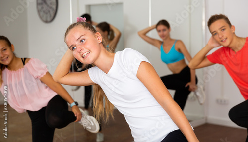Smiling teen girl enjoying while training movements of modern group dance in choreography class