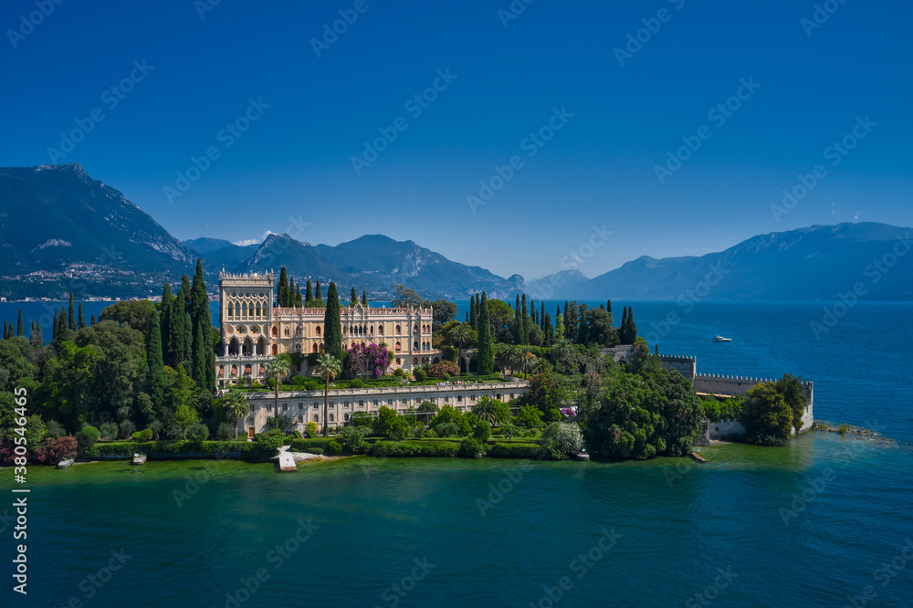 Is the biggest island on Lake Garda. The Venetian neo gothic Villa Borghese Cavazza. Aerial view of the island Garda, Lake Garda, Italy Aerial photography. In the background Alps, blue sky.