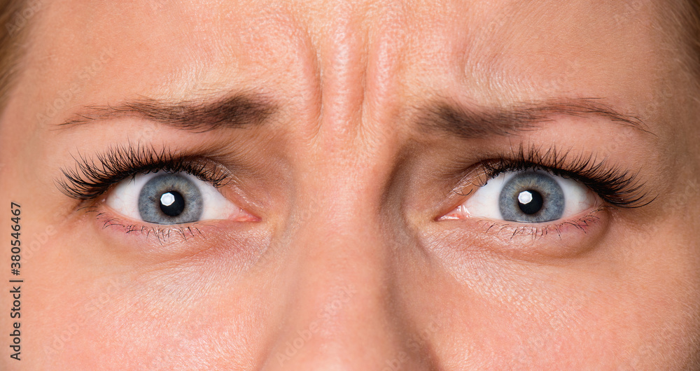Close-up scared face of beautiful young woman with beautiful blue eyes and big pretty eyelashes and eyebrows. Macro of human eyes - surprise or shock, looking at camera. Close-up scared face of beautiful young woman with beautiful blue eyes and big pretty eyelashes and eyebrows. Macro of human eyes - surprise or shock, looking at camera.