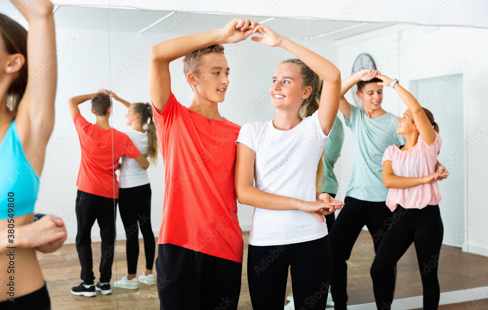Fototapeta Grupa szczęśliwych, wesołych, uśmiechniętych nastoletnich chłopców i dziewcząt trenujących ruchy powolnego fokstrota w studiu tańca z trenerką