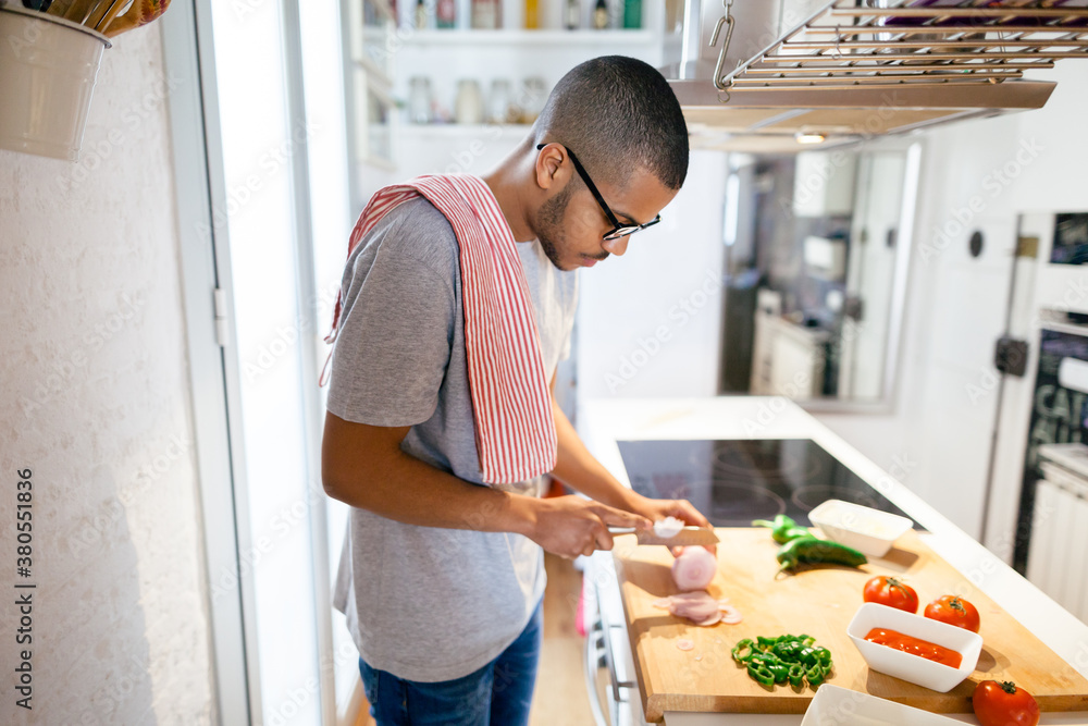 Side view of a latin man cutting onion to make an Italian pizza at home. Side view of a latin man cutting onion to make an Italian pizza at home.
