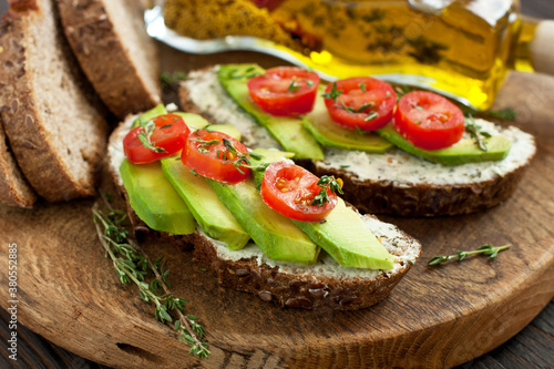 Healthy toast with cream cheese, avocado, cherry tomatoes on rustic wooden table. Selective focus, close up