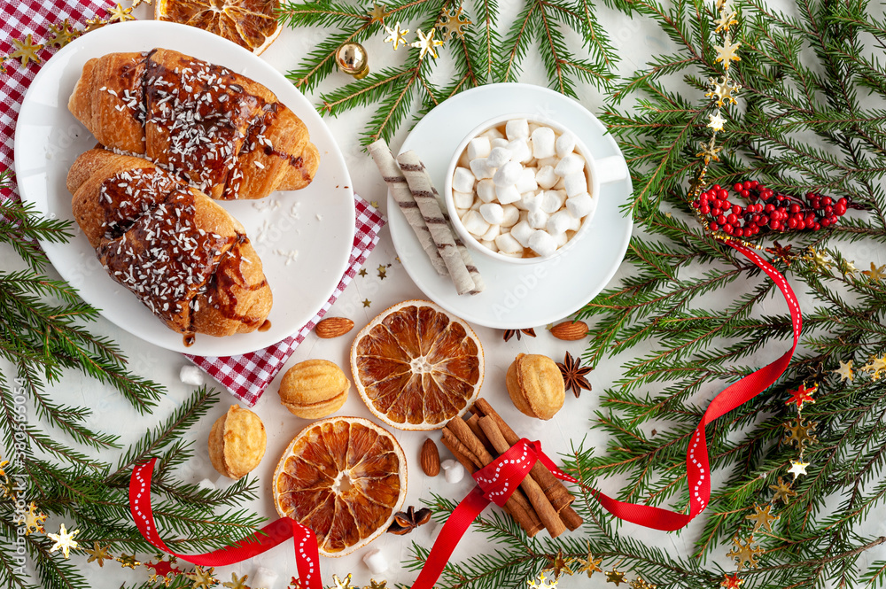 Christmas breakfast. Christmas morning. A cup of cocoa with marshmallows and croissants on a light concrete background with a branch of decorated Christmas tree. Place for text. View from above. Christmas breakfast. Christmas morning. A cup of cocoa with marshmallows and croissants on a light concrete background with a branch of decorated Christmas tree. Place for text. View from above.