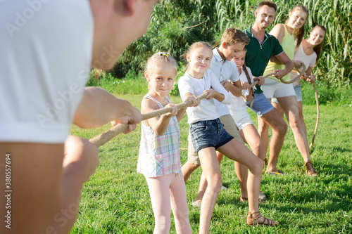 portrait of kids with parents playing active games in summer park, tugging war