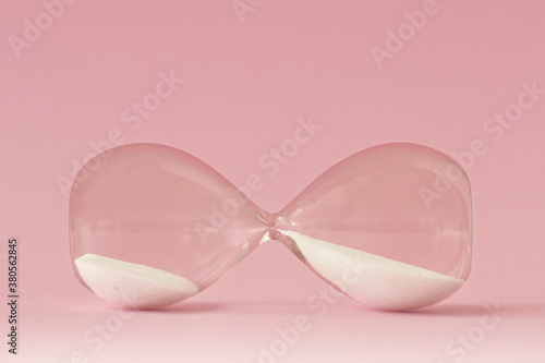 Hourglass lying on pink background - Concept of time and woman photo