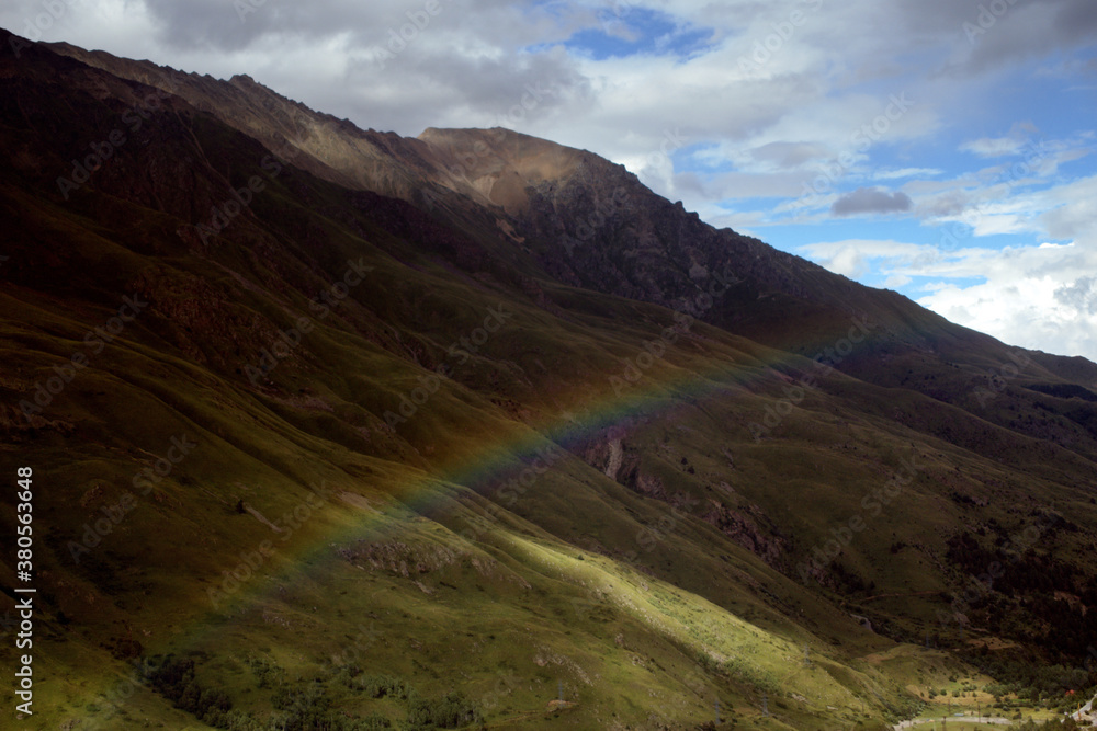 Obraz premium Rainbow over a green valley surrounded by mountains. Caucasus, Russia.