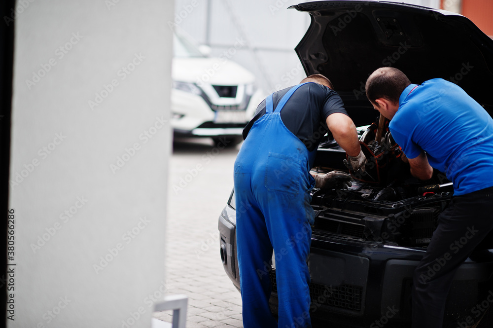Car repair and maintenance theme. Two mechanics in uniform working in auto service, checking engine.