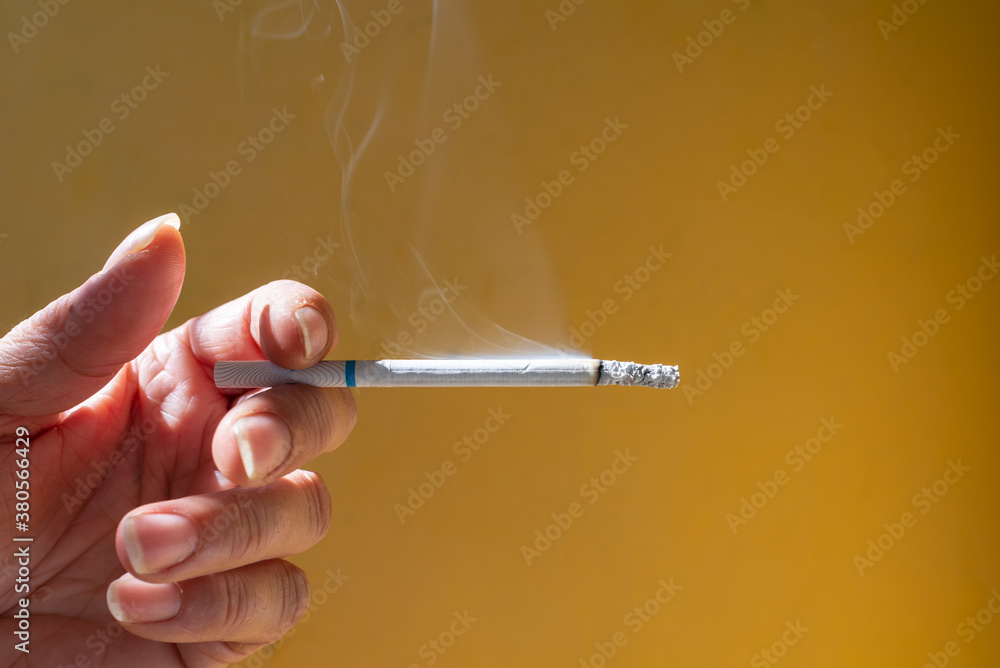 Stop smoking.Woman Hand holding a smoldering cigarette against the dark ugly wall Stop smoking.Woman Hand holding a smoldering cigarette against the dark ugly wall