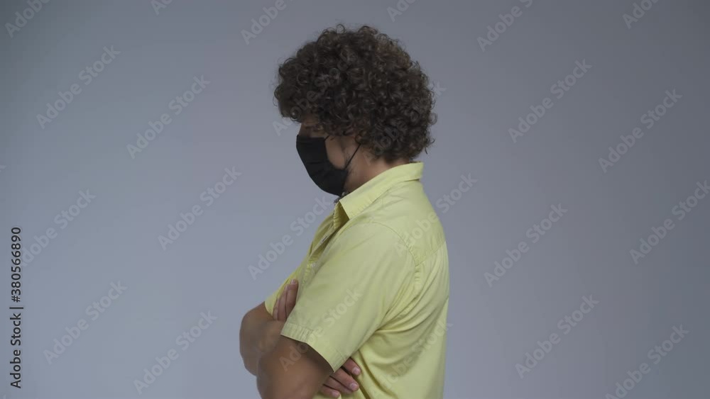 Curly man stands in a profile in a medical mask. Guy crossed his arms on his chest and turns discontentedly into the camera. High quality. Curly man stands in a profile in a medical mask. Guy crossed his arms on his chest and turns discontentedly into the camera. High quality.