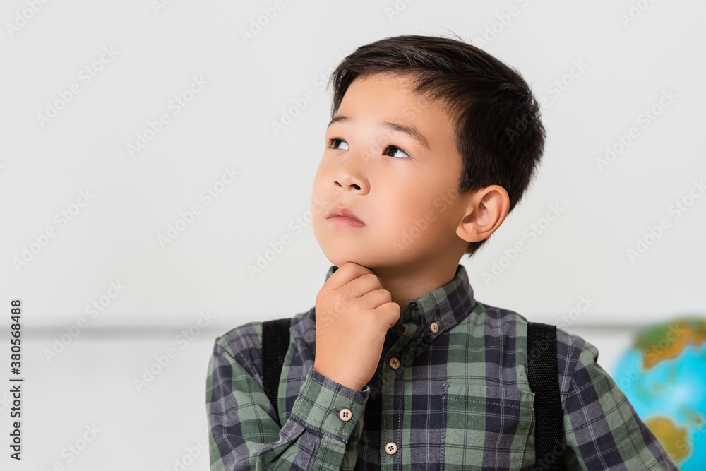 Pensive asian schoolboy looking away in classroom Pensive asian schoolboy looking away in classroom