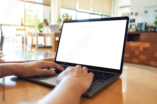 Mockup image of a woman using and typing on laptop computer keyboard with blank white desktop screen on wooden table