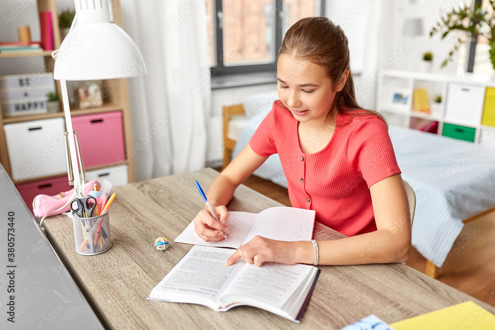 children, education and learning concept - happy smiling student teenage girl with book writing to notebook at home