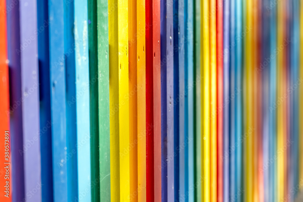 Part of wooden, rainbow colorful painted fence  on a sunny hot summer day in a city park.