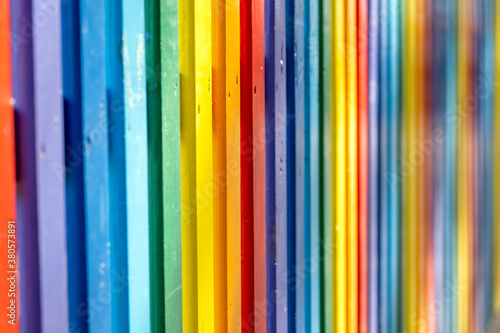 Part of wooden, rainbow colorful painted fence on a sunny hot summer day in a city park.