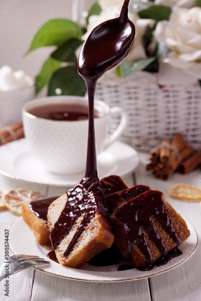 Chocolate icing pouring on freshly baked homemade cake lying on a white saucer Chocolate icing pouring on freshly baked homemade cake lying on a white saucer