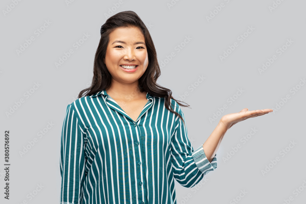 people, gesture and presentation concept - happy asian young woman holding something on hand over grey background people, gesture and presentation concept - happy asian young woman holding something on hand over grey background