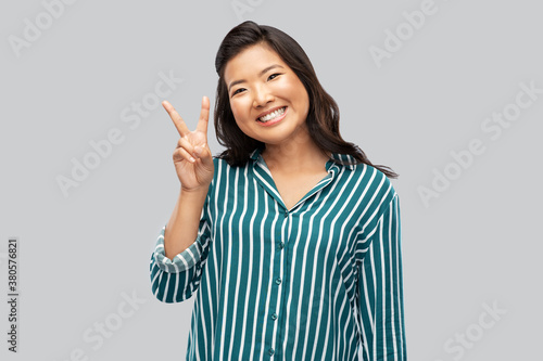 people, success and gesture concept - happy asian young woman showing peace hand sign over grey background
