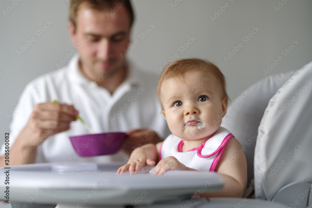 Father feeding baby daughter in high chair Father feeding baby daughter in high chair