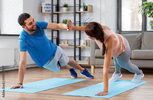 fitness, sport, training and healthy lifestyle concept - happy couple make high five in side plank at home